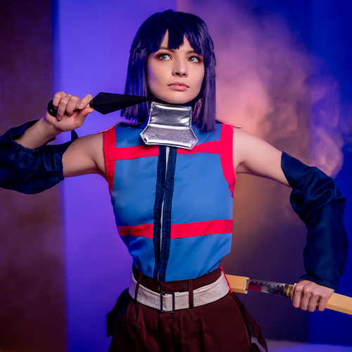 Akatsuki cosplay from Log Horizon. The model poses confidently, holding a kunai at her neck with her right hand while gripping a sword with her left. She wears a blue and red ninja outfit, and her intense expression is enhanced by the atmospheric blue and purple lighting with mist in the background.