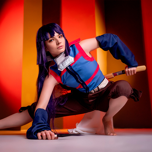 Akatsuki cosplay from Log Horizon. The model is crouched in an action pose, gripping a sword in her left hand and a kunai in her right. Her intense gaze and ready-to-strike stance are complemented by the dramatic red and orange lighting in the background, adding a sense of urgency and movement to the scene.