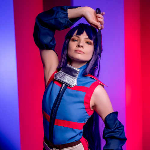 Akatsuki cosplay from Log Horizon. The model strikes an elegant pose, holding a kunai above her head with her right hand while her left hand rests on her waist. She wears a blue and red ninja outfit, and the vibrant lighting in the background adds depth and drama to the scene.