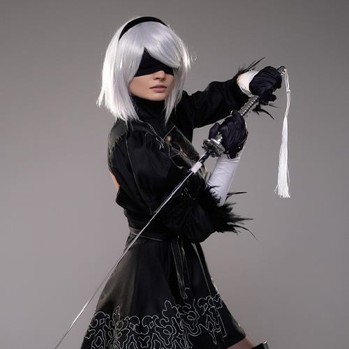 Dynamic 2B cosplay from Nier: Automata, poised in mid-action with a drawn sword, ready for battle, capturing the character's strength and agility.