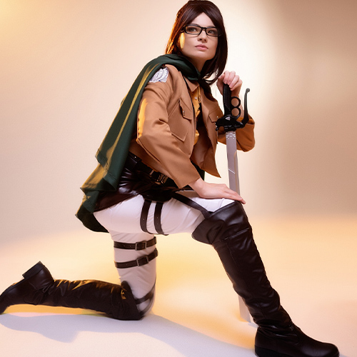 Hanji Zoe cosplay from Attack on Titan, kneeling in an action-ready pose with her blade in hand, wearing the iconic Survey Corps uniform and glasses, illuminated by a warm light