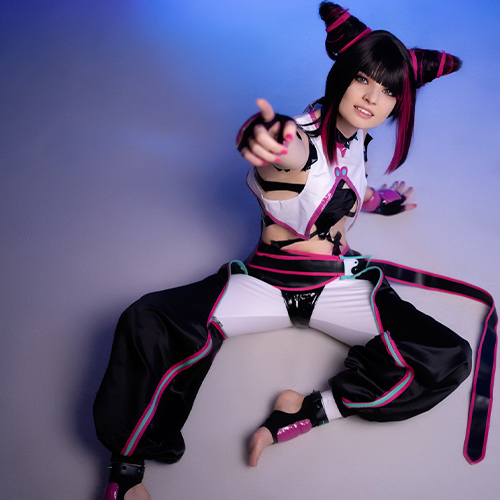 Cosplayer dressed as Juri Han from Street Fighter, sitting on the ground with her legs spread out, reaching forward in a dynamic pose. The lighting is a mix of blue and purple, highlighting her playful yet fierce expression and the intricate details of her black, pink, and white outfit