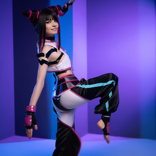 Cosplayer in a dynamic pose dressed as Juri Han from Street Fighter, balancing gracefully on one leg with the other leg bent. The vibrant purples and blues in the background match the accents on her costume, which features a striking black, white, and pink color palette. The cosplay captures Juri's fierce yet playful demeanor