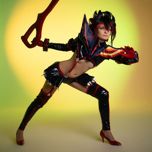 A dramatic pose by Ryuko Matoi from Kill la Kill, as she prepares to fight with a pair of giant red scissors. Senketsu's latex suit sparkles in the bright lights, and the sharp dynamics of her movements add to the presence and power of the character. Red heels complete the look, and the colorful background adds depth to the dramatic scenario.