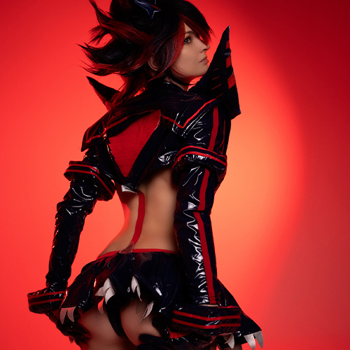 Back view of a striking Ryuko Matoi cosplay from Kill la Kill, with the red and black Senketsu costume gleaming under the light. The bold contrast of the dark latex outfit against the red backdrop emphasizes the sharp, angular design of the outfit, showcasing the detailed craftsmanship of the character’s iconic look