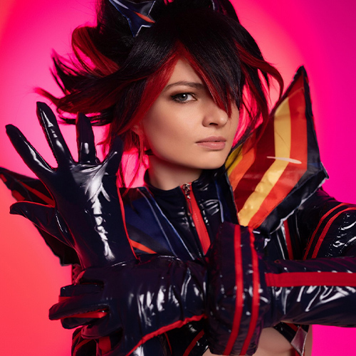 Close-up of Ryuko Matoi cosplay with intense gaze and striking pose. The vibrant red and black costume details shine under the bold pink lighting, emphasizing the character's fierce personality and signature style from Kill la Kill