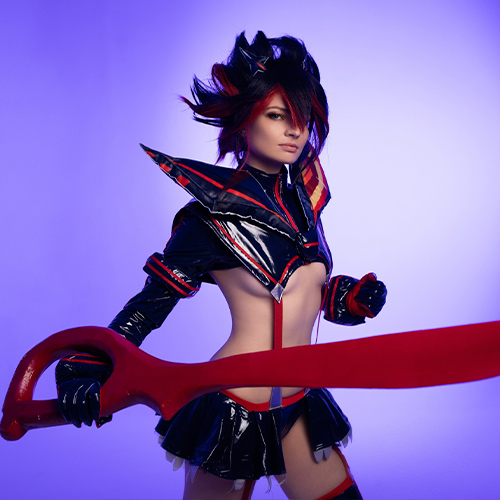 Dynamic Ryuko Matoi cosplay wielding the iconic red Scissor Blade. The bold purple backdrop contrasts with the character’s black and red outfit, showcasing the fierce energy and style from Kill la Kill