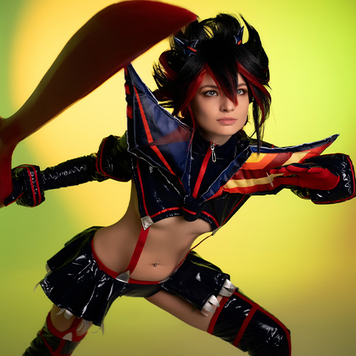 Dynamic Ryuko Matoi cosplay wielding her iconic scissor blade in a powerful action pose. The striking red and black outfit contrasts boldly against a green-yellow backdrop, showcasing the character's fierce energy and determination