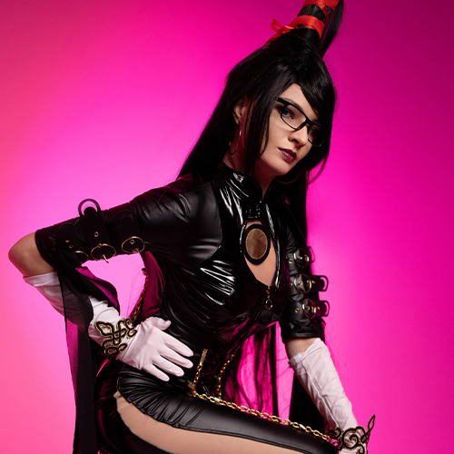 Bayonetta cosplay posed in a sleek action stance, showcasing the black latex outfit adorned with gold chains and intricate details, against a vivid pink backdrop. The high ponytail and stylish glasses, combined with the white gloves and red accents, complete the character's powerful look