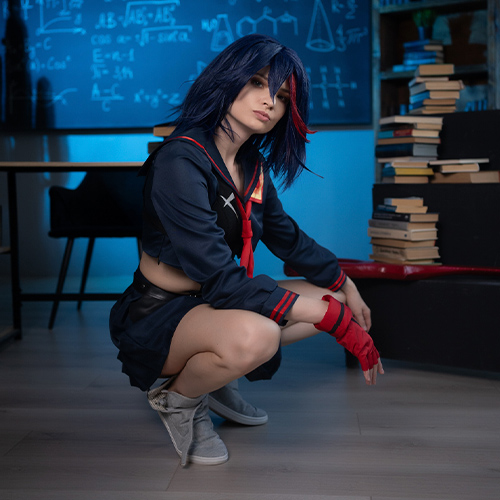 Ryuko Matoi cosplay in a school classroom setting, crouching in front of a chalkboard filled with scientific equations. The cosplayer wears Ryuko's iconic blue and red sailor uniform, complete with red gloves, embodying a fierce and determined expression. The background features shelves of books and portraits of famous scientists