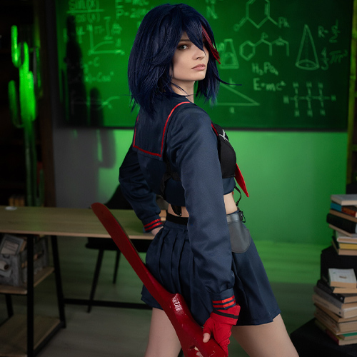 Ryuko Matoi cosplay standing in a school setting with a confident stance, holding her large red scissor blade behind her. The cosplayer wears a navy blue sailor uniform with red accents and a serious expression, capturing Ryuko’s determined personality. The classroom background includes a chalkboard filled with scientific diagrams and green lighting that adds an intense atmosphere