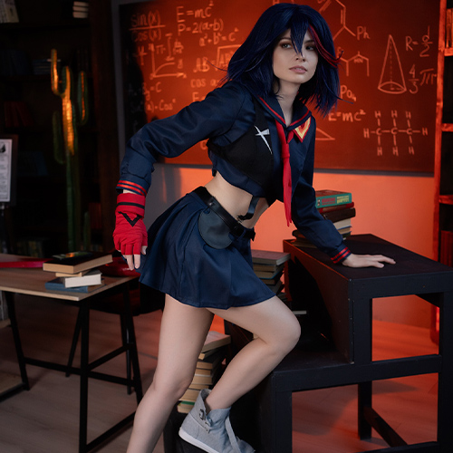 Ryuko Matoi cosplay character posed dynamically in a classroom setting, leaning on stacked desks with a serious expression. Dressed in her iconic navy blue and red-trimmed school uniform with matching fingerless gloves, the character stands amid books and scientific sketches on a chalkboard, highlighted by warm orange lighting that adds intensity to the scene