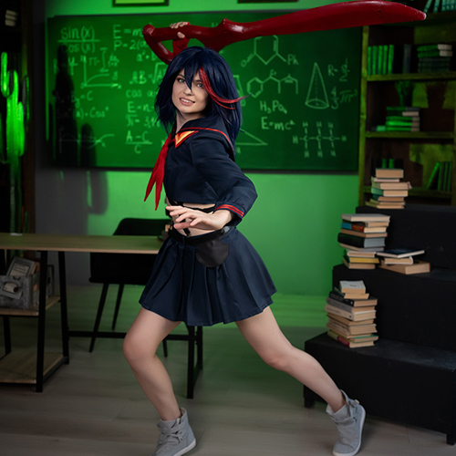 Ryuko Matoi cosplay character in an action pose within a classroom setup, brandishing a large red scissor blade. Dressed in a dark school uniform with a red necktie, she strikes a dynamic stance that conveys movement, surrounded by a green-lit background of chalkboard equations and stacked books, enhancing the intense academic ambiance