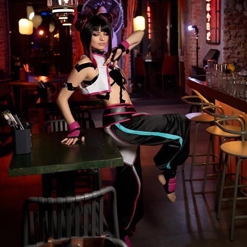 Juri Han sits confidently on a table, capturing her fearless and unpredictable attitude. Her iconic hair buns, highlighted by pink streaks, and her bold, edgy attire—complete with black, pink, and turquoise accents—stand out under the ambient neon lights. The setting, reminiscent of an urban, futuristic bar, complements Juri's rebellious and chaotic vibe, adding depth to her intense and dynamic character