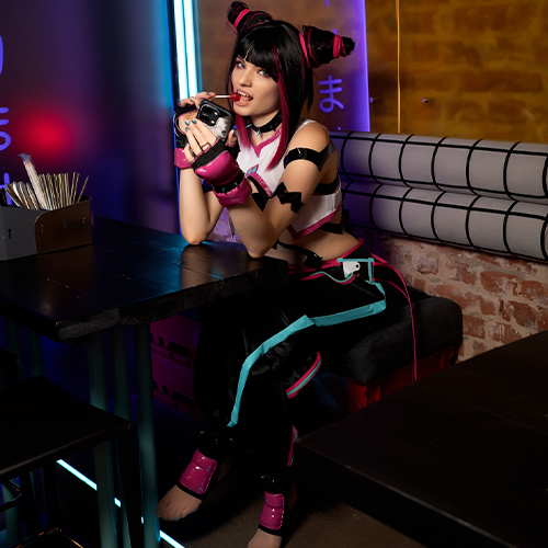 Juri Han lounges at a table with a mischievous expression, holding a drink while her tongue playfully touches the straw. Her iconic dual-bun hairstyle and black-and-pink outfit stand out under the neon lights, which add a vibrant atmosphere to the scene. The setting, with its Japanese signage and cozy vibe, complements her edgy and rebellious character. Her relaxed yet intense pose captures Juri's unpredictable and playful nature