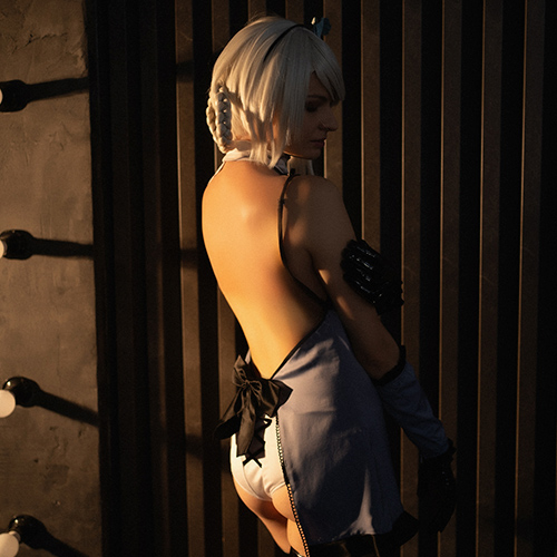 Kaine from Nier: Replicant stands with her back turned, highlighting the delicate, open design of her outfit. The warm, low lighting casts dramatic shadows, accentuating the contours of her figure and creating a mood of quiet intensity. Her silver hair is styled simply, with a braid adding a touch of elegance, while her pose conveys a sense of vulnerability mixed with defiance. This shot captures Kaine’s complexity, combining softness with strength in a powerful tribute to her character.