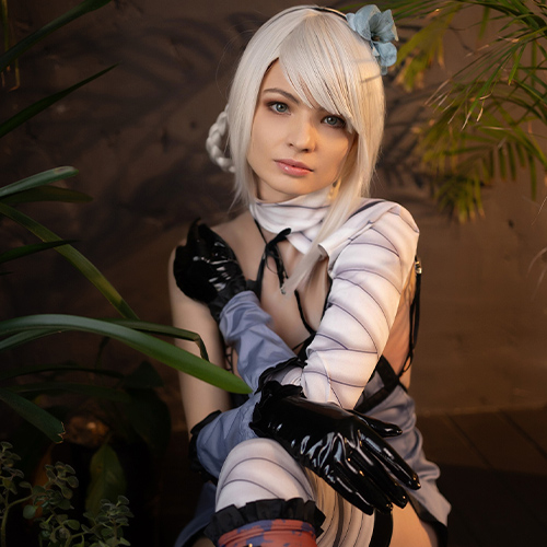 Kaine from Nier: Replicant sits amidst lush green plants, her soft gaze inviting a rare moment of vulnerability. The earthy tones and shadows around her frame her delicate features, while the intricate details of her bandaged arm and black gloves highlight her resilient yet wounded spirit. This close-up shot captures Kaine's inner conflict and strength, blending her fierce character with a serene, almost introspective ambiance.