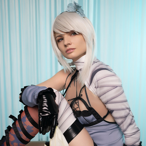 Kaine from Nier: Replicant sits poised, embodying her fierce yet vulnerable essence against a soft, blue background. The gentle lighting highlights her iconic bandaged arm and intricate outfit details, adding depth to her complex character. The serene setting contrasts with her warrior spirit, capturing the duality that fans of the series cherish.