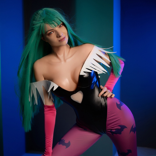 Morrigan Aensland from Darkstalkers leans forward with a playful, yet mischievous expression, her vibrant green hair cascading down her shoulders. The sleek black bodysuit with its signature heart cutout and the pink bat-patterned leggings accentuate her iconic look. The blue and green background lighting highlights her flirtatious and confident aura, capturing the essence of this beloved succubus character.