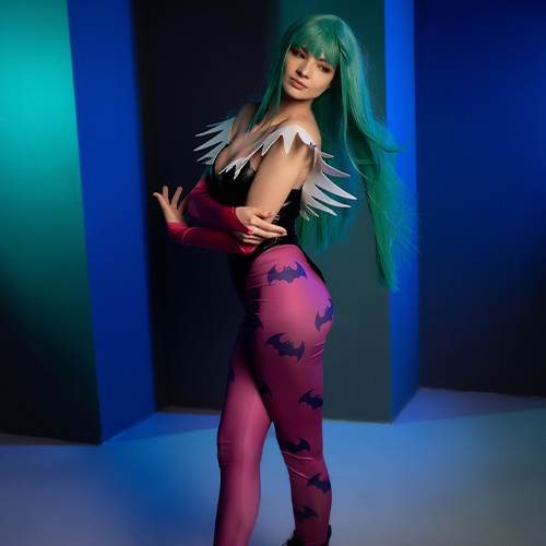 Morrigan Aensland strikes a poised and confident stance, her iconic green hair flowing against a cool-toned backdrop. The cosplay accentuates her bat-winged leggings and signature off-shoulder bodysuit, detailed with her pink gloves and wing-like accents. The subdued lighting adds a mysterious allure, capturing Morrigan’s captivating and fierce essence from Darkstalkers.