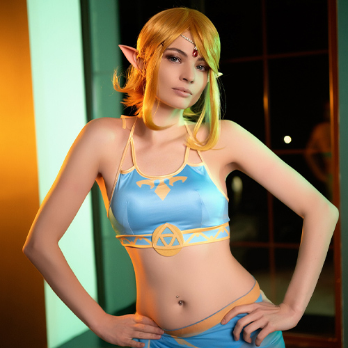 An enchanting Zelda cosplay that blends elegance with allure, showcasing a captivating female version of the iconic character. The detailed costume highlights her toned abs and slim waist, while her confident stance and sultry expression add a sexy twist to the classic look. The cosplay features Zelda’s recognizable symbols and color palette, paired with an eye-catching slit skirt that reveals just enough leg for a tantalizing effect. This gender-bender take on Zelda, complete with pointed ears and a radiant headpiece, brings a fresh, seductive energy to the beloved character, making this portrayal both iconic and unforgettable