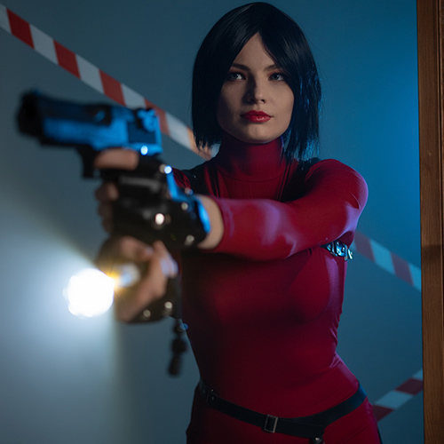 Ada Wong cosplay from Resident Evil showcasing her fierce and tactical side, with a striking red dress and black harness accents. The dynamic pose with a gun aimed forward emphasizes her bold, action-ready demeanor, while the intense lighting adds drama to the scene. The character's sharp bob hairstyle and confident expression perfectly embody Ada’s mysterious and fearless personality.