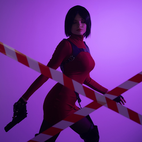 Ada Wong cosplay from Resident Evil in a striking and dynamic pose, accentuated by a bold purple backdrop. The iconic red dress emphasizes her sleek silhouette, paired with her tactical gloves and holstered weapon, capturing her action-ready stance. The red-and-white caution tape adds a layer of intrigue and danger, mirroring Ada's enigmatic and resourceful personality. This cosplay brilliantly embodies the elegance and strength of one of gaming’s most memorable femme fatales.