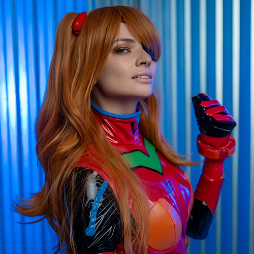 Asuka Langley Soryu cosplay from Neon Genesis Evangelion, showcasing her confident and fiery personality. The vibrant red plugsuit is perfectly recreated, with intricate green and orange detailing that stays true to the anime's original design. Her iconic orange-red twin tails and hair clips complete the look, emphasizing her bold character. The blue metallic background provides a dynamic and futuristic contrast, highlighting the glossy finish of the plugsuit. This portrayal captures Asuka's essence as a determined and spirited EVA pilot, making it a standout representation of this beloved anime character.