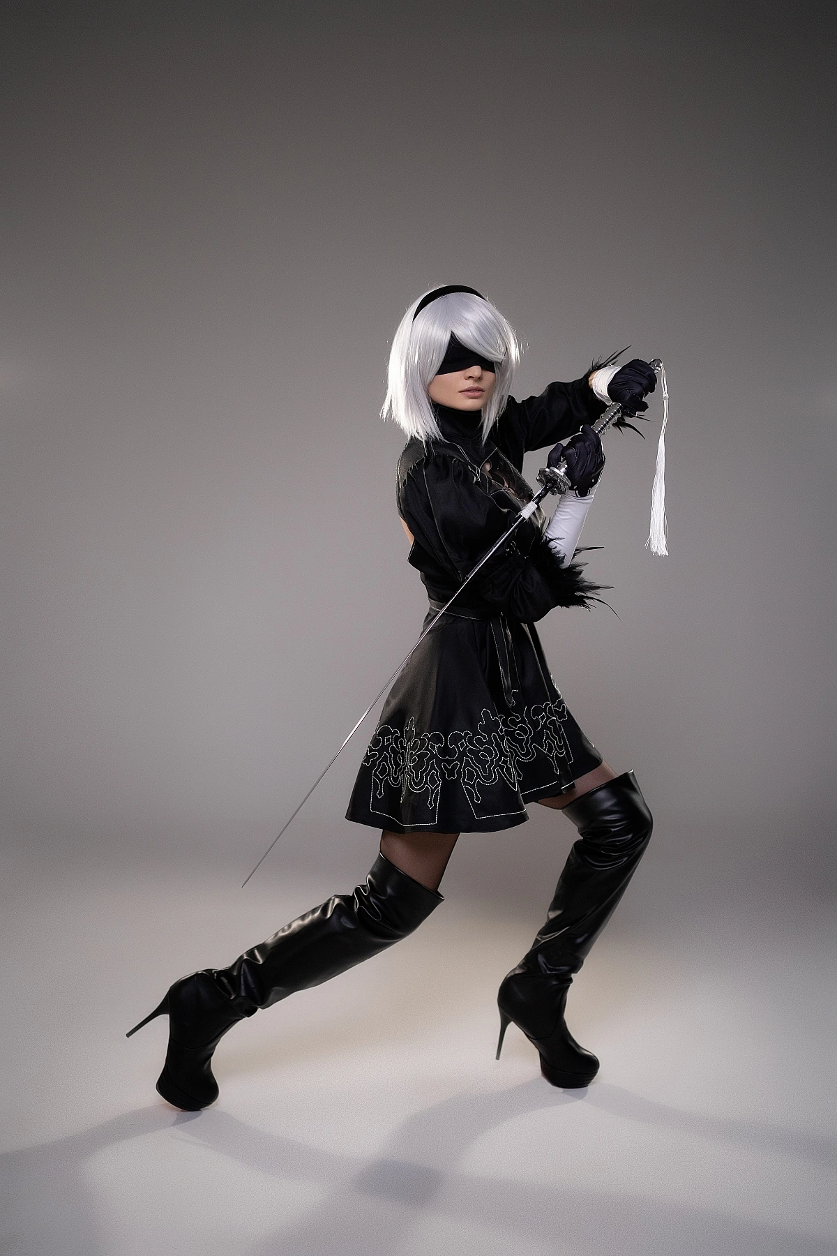 2B NieR Automata cosplay action pose with katana lunge attack, silver hair, blindfold, black dress, dynamic studio shot