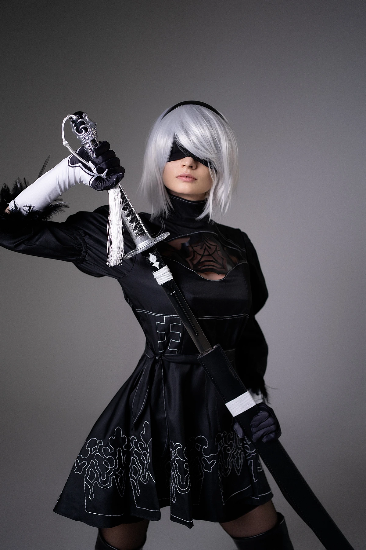 Close-up 2B NieR Automata cosplay portrait with blindfold and katana detail, silver bob wig, embroidered black dress