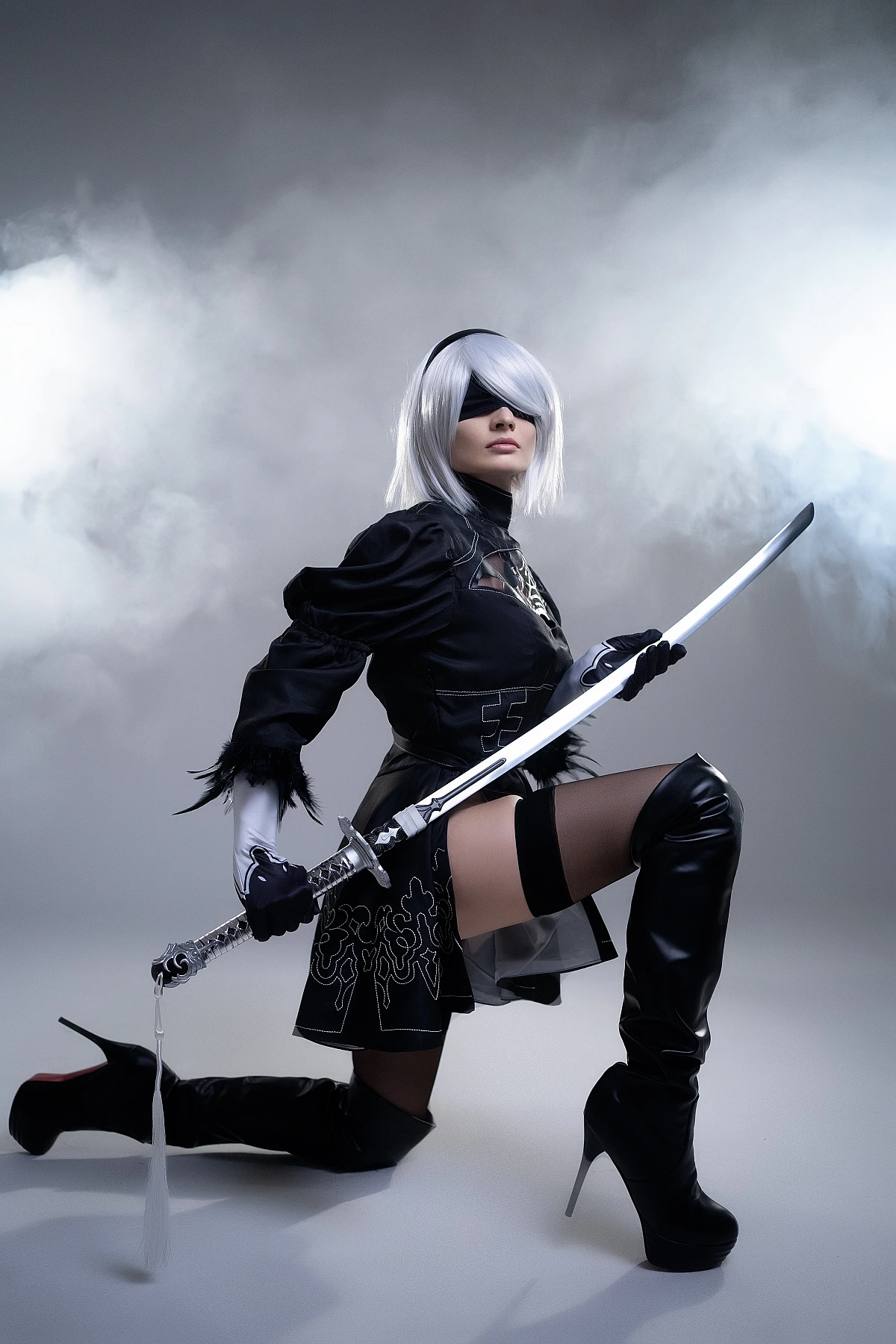 2B cosplay kneeling pose with katana in atmospheric smoke, silver bob wig, black blindfold, NieR Automata YoRHa costume