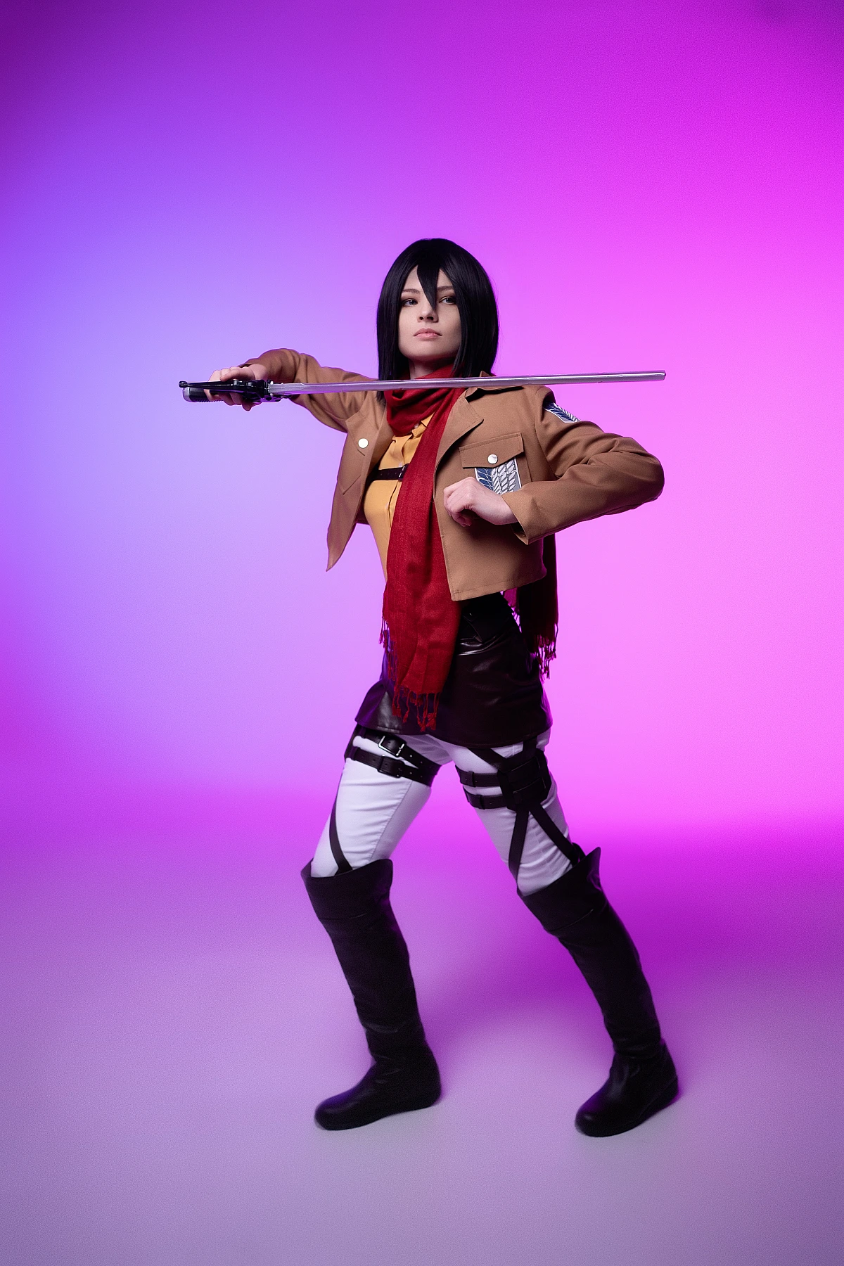 mikasa ackerman full-body cosplay with extended blade pose showing complete survey corps costume against purple-pink backdrop