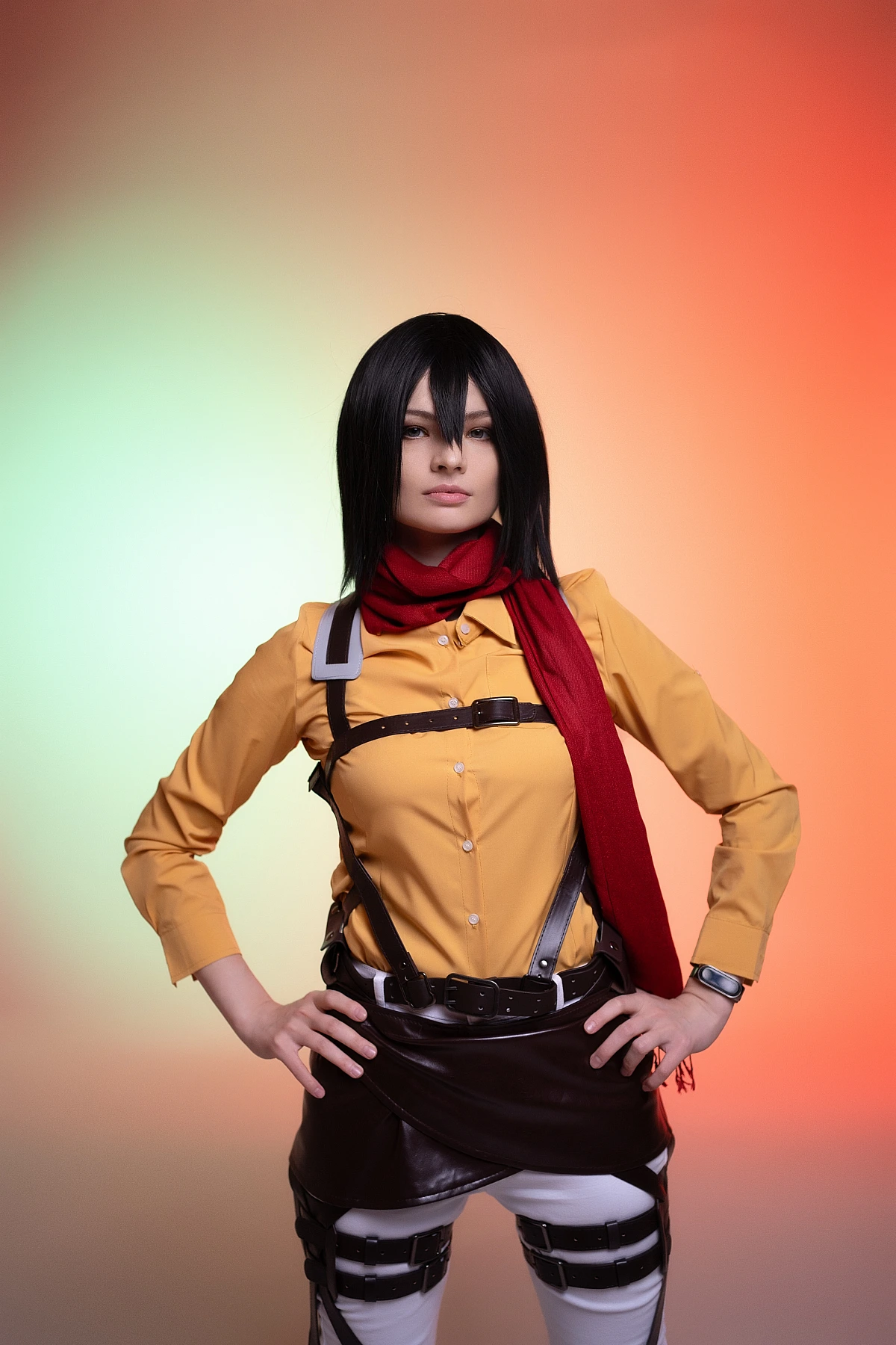 mikasa ackerman cosplay confident pose with hands on hips showing red scarf and odm harness against gradient backdrop