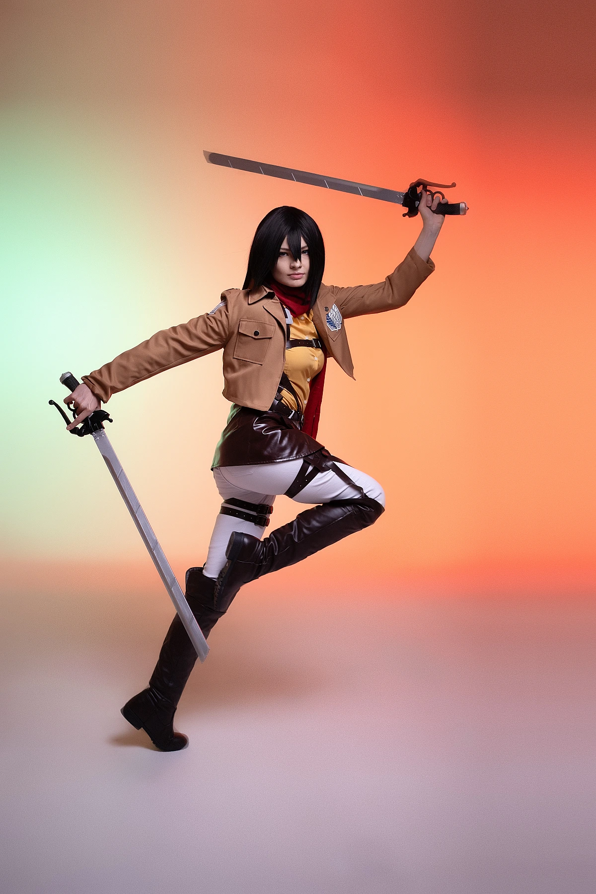 mikasa ackerman cosplay mid-air leap with dual blades extended and red scarf trailing against warm studio gradient