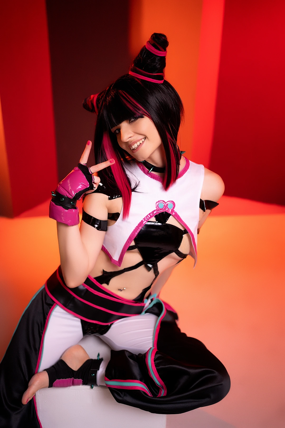 Juri Han cosplayer smiling on white cube, barefoot, playful hand gesture, warm orange neon columns, horn buns, Street Fighter
