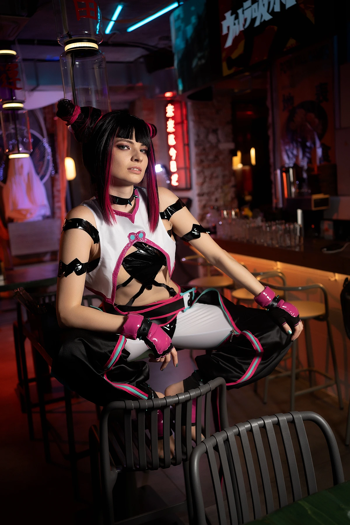 Wide-angle Juri Han cosplay shot showing low crouch pose in full neon bar environment with glowing signs and bar stools
