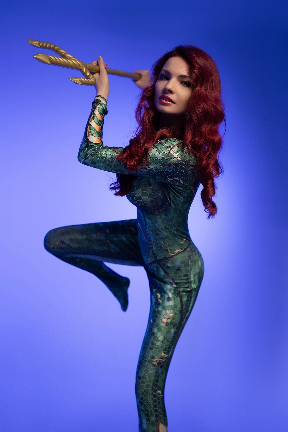 Dynamic Mera cosplay balancing on one leg with raised trident in emerald scale bodysuit