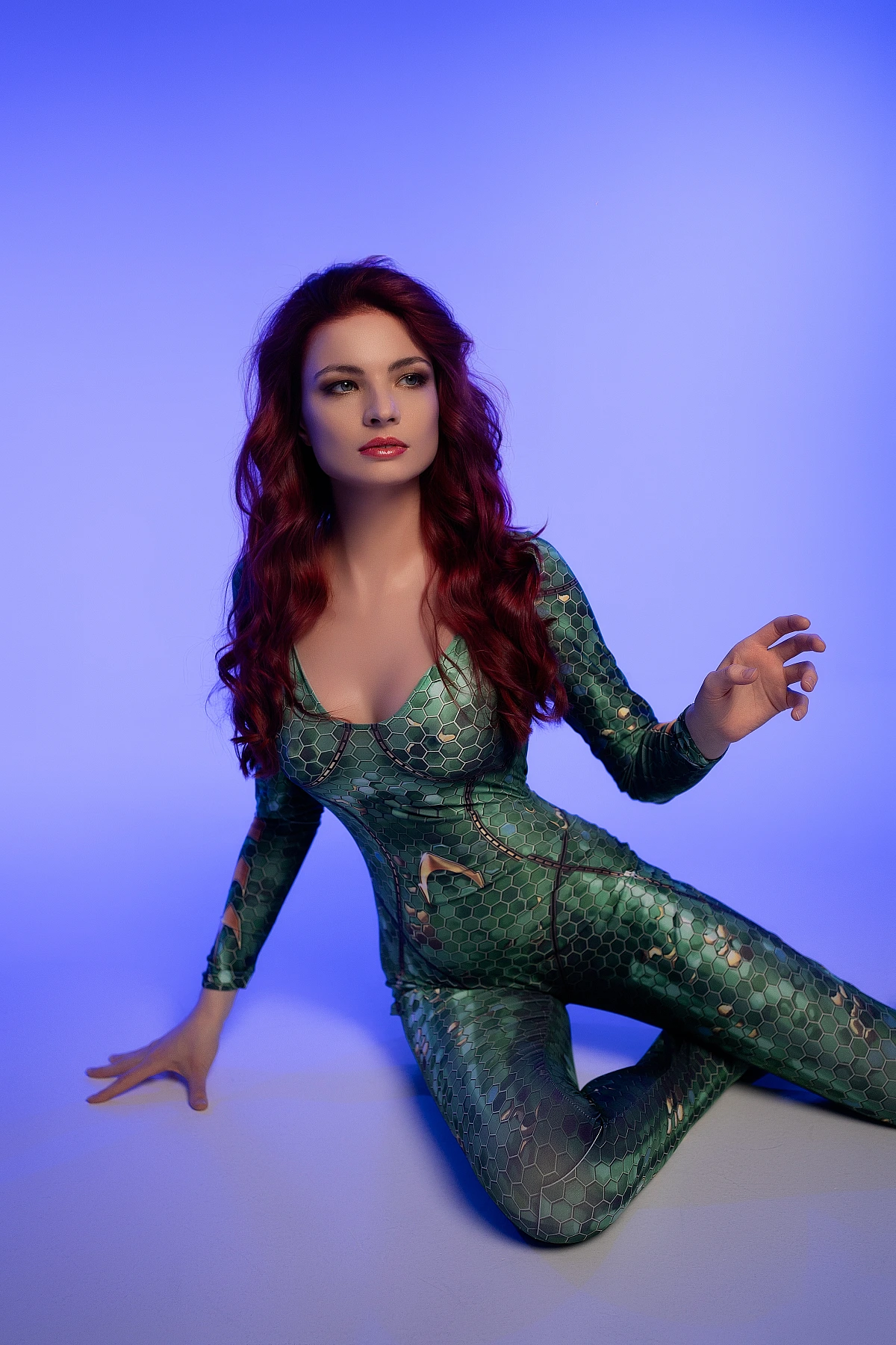 Seated diagonal Mera cosplay pose in emerald scale bodysuit with tranquil blue lighting