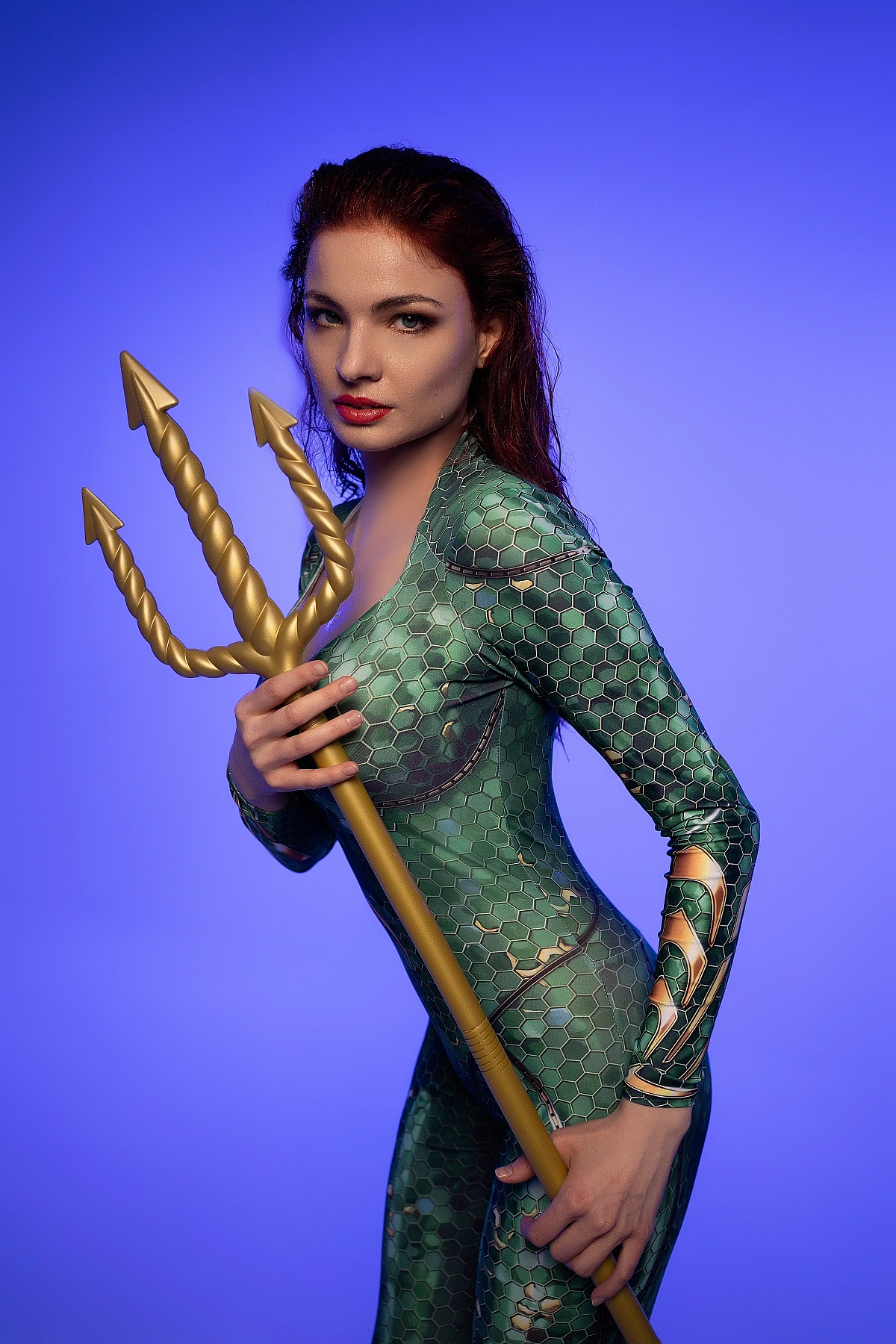 Close portrait Mera cosplay holding golden trident with intense gaze in emerald scale bodysuit