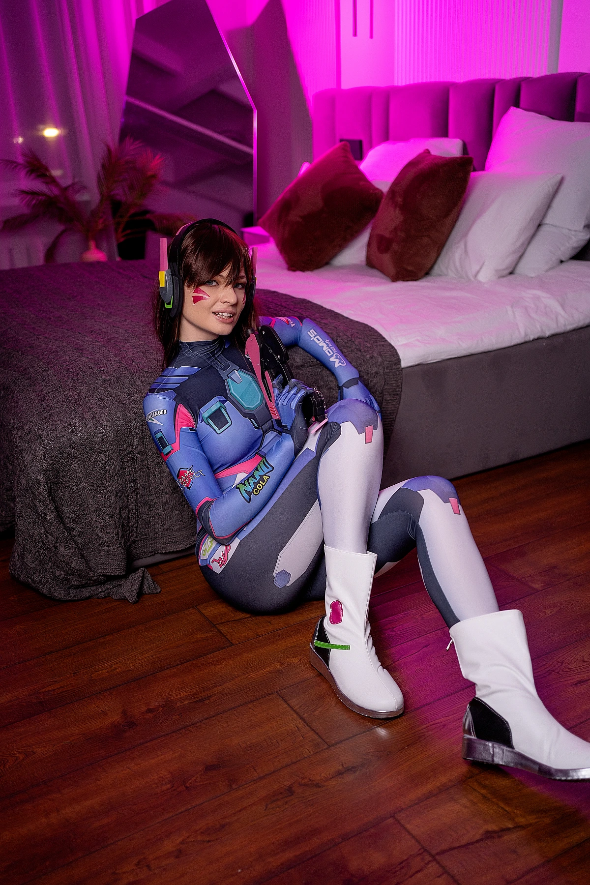 D.Va cosplay casual bedroom pose, pink neon lighting, cosplay boots visible, relaxed smile, Overwatch gaming character