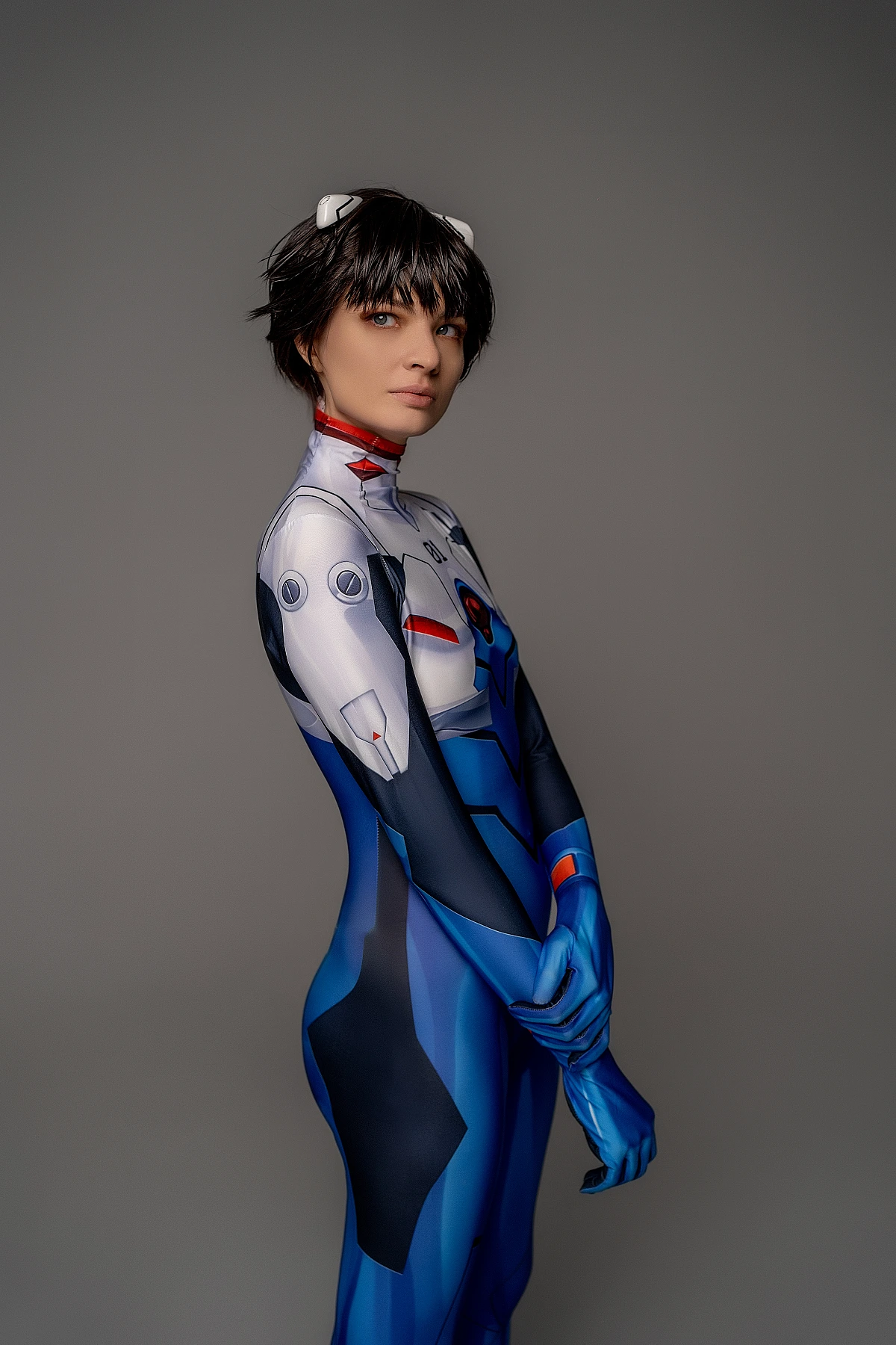 androgynous Shinji Ikari cosplay side profile, fitted blue bodysuit, slim silhouette, anime crossplay photography, gray studio