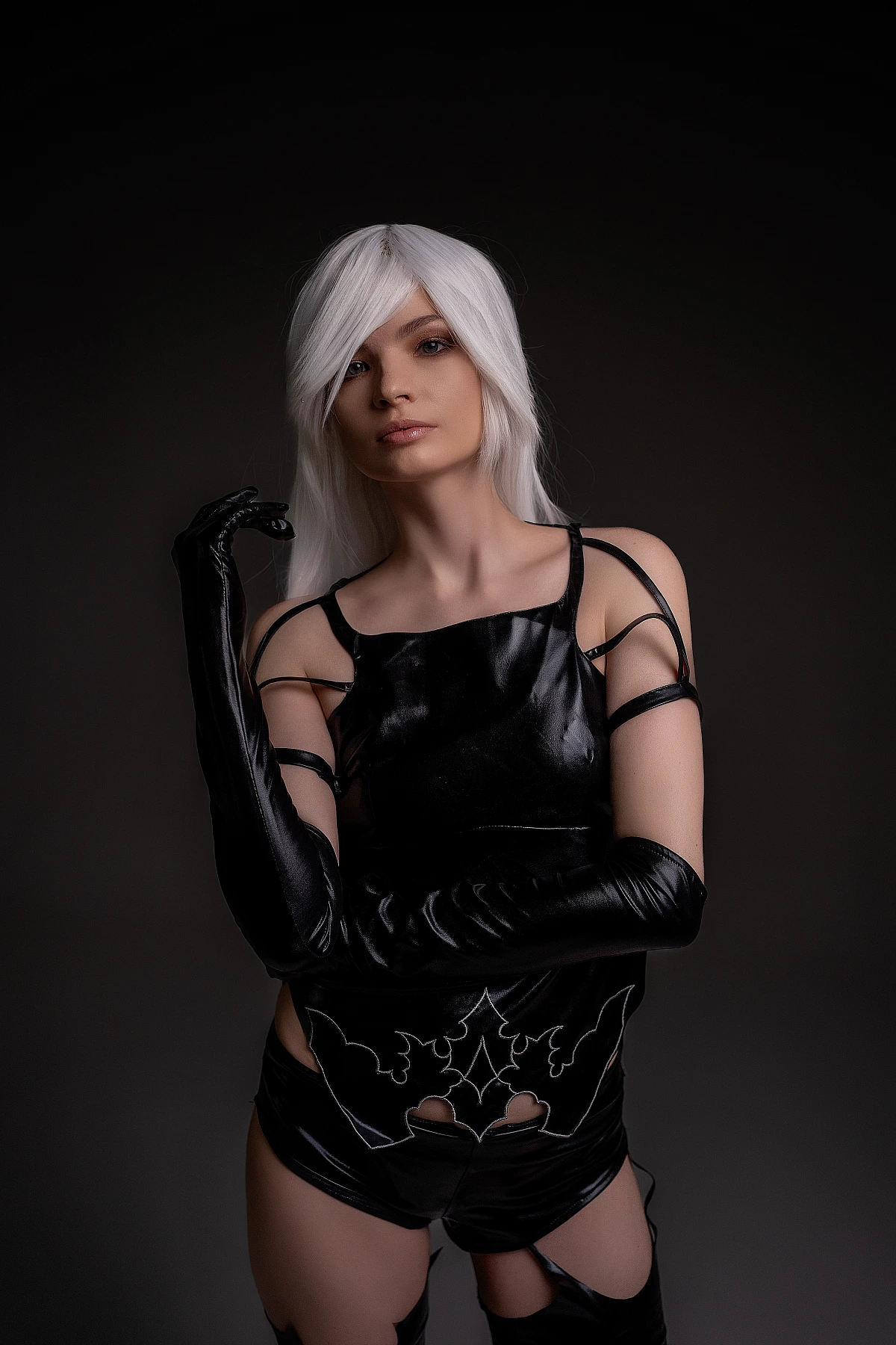 A2 cosplay NieR Automata athletic build defined arms fitted black outfit white hair calm gaze dark studio battle-ready