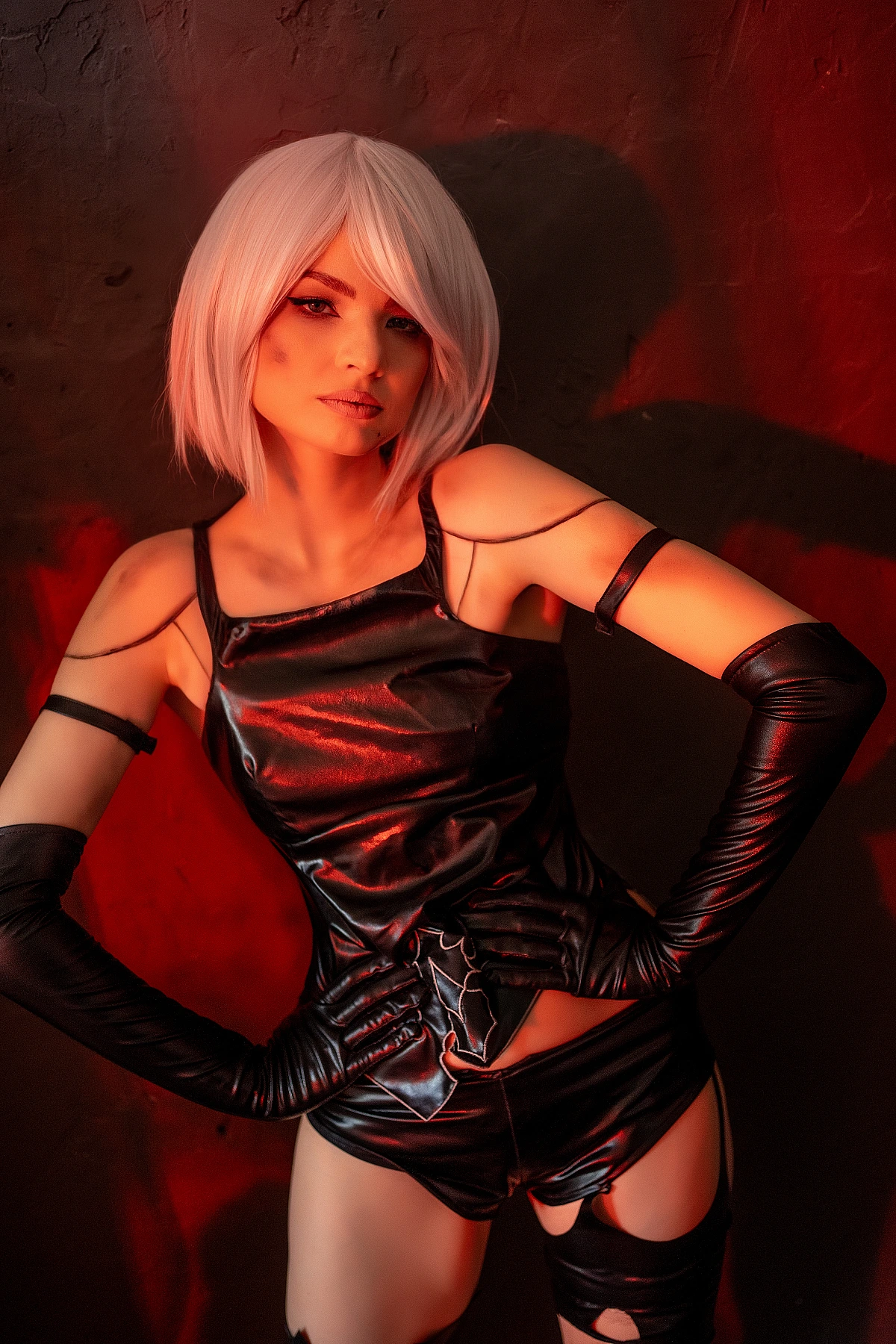 A2 NieR Automata cosplay red light portrait, hands on hips dominant pose, glossy black latex outfit, white bob hair, dark background, saturated dramatic lighting