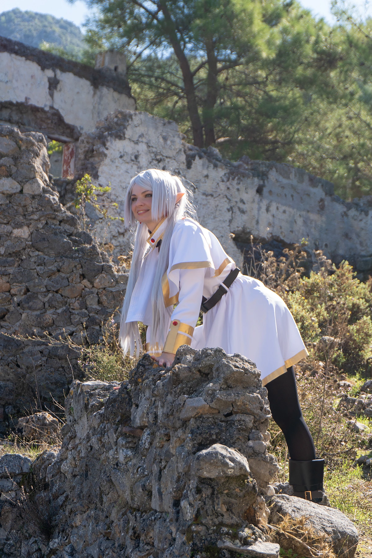 Frieren cosplay leaning forward stone ruins silver hair elf ears white mage outfit forested ruin background daylight Sousou no Frieren