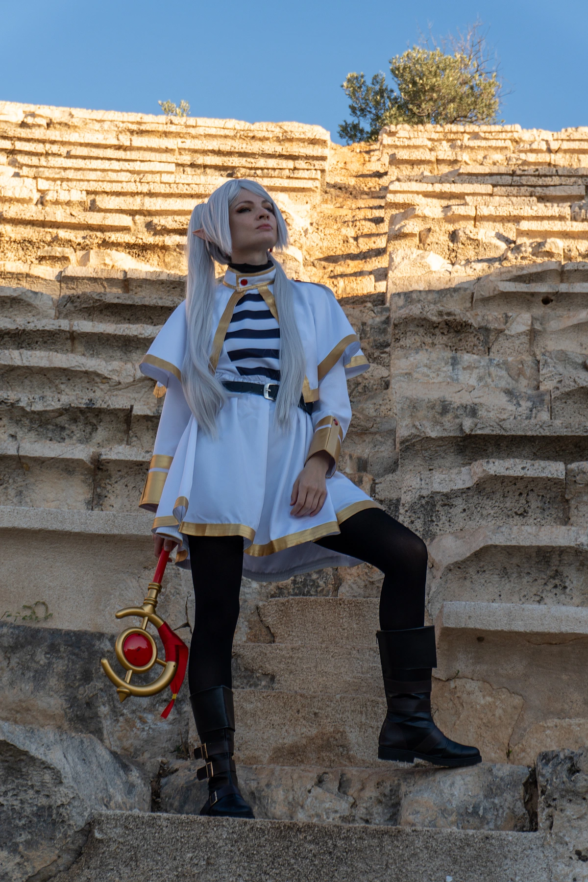 Frieren cosplay standing stone steps staff in hand silver hair elf ears white gold mage dress ancient ruin open sky