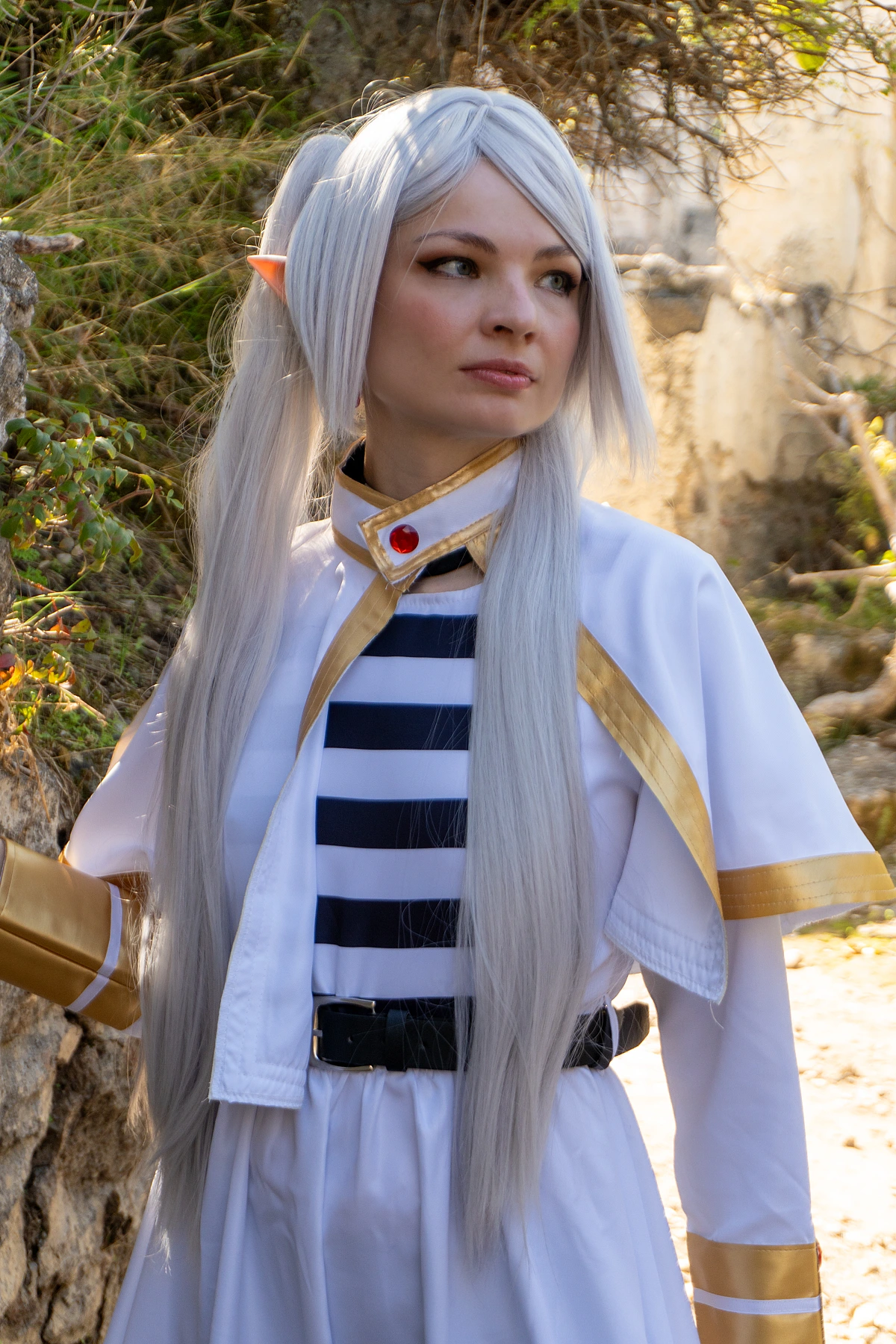 Frieren cosplay close-up portrait calm distant gaze silver hair elf ears white gold outfit soft forest background