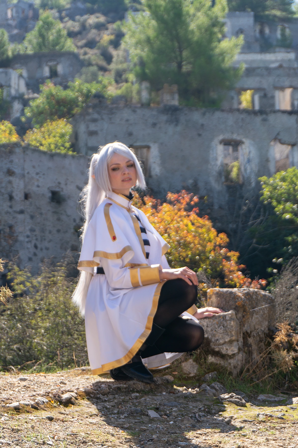 Frieren cosplay crouching weathered stone silver hair elf ears white gold mage costume autumn foliage ancient ruins daylight