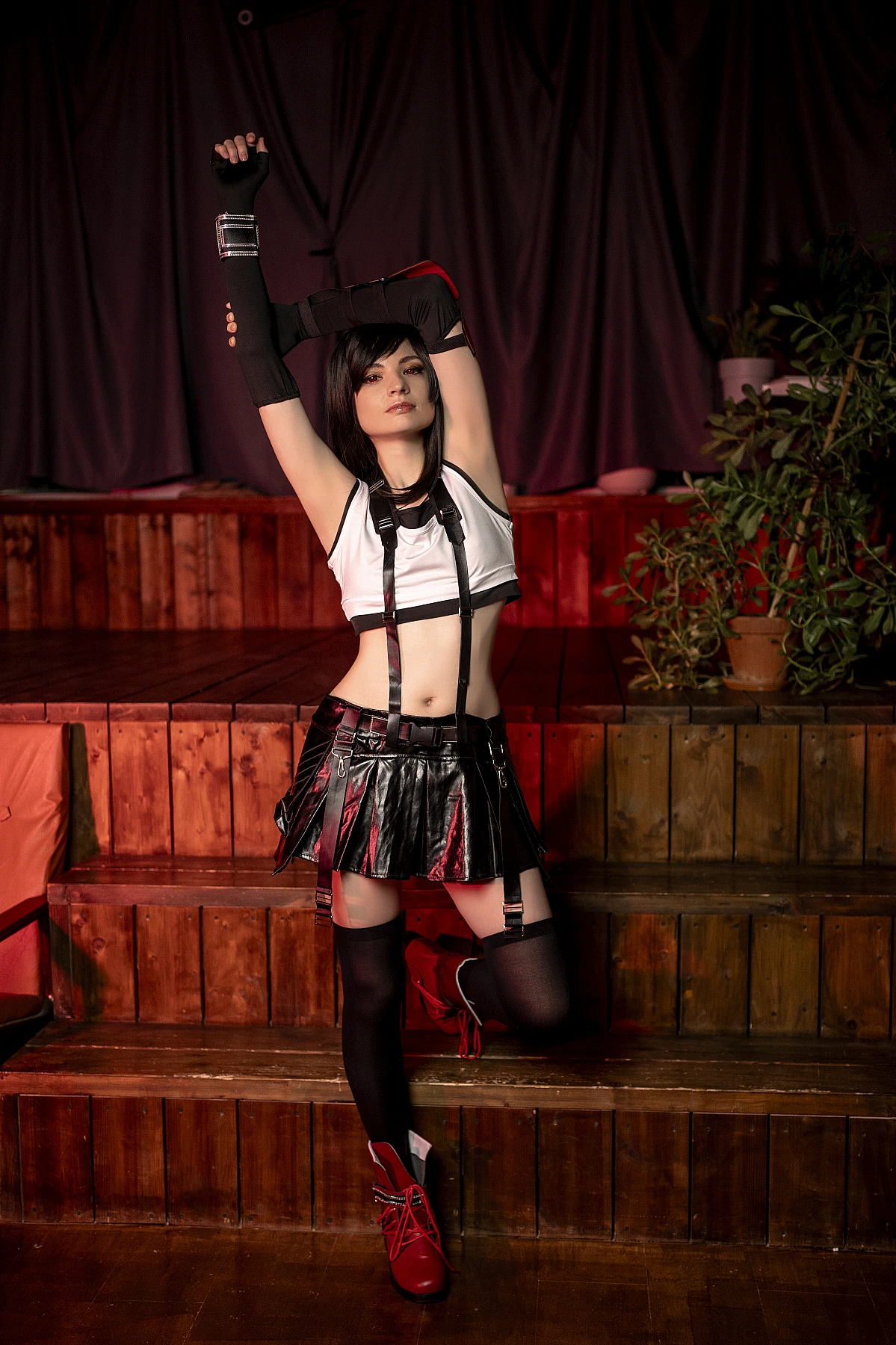 Tifa Lockhart FF7 cosplay overhead stretch pose on gym steps, athletic physique, black skirt with suspenders, thigh-high stockings, red boots, dramatic warm lighting