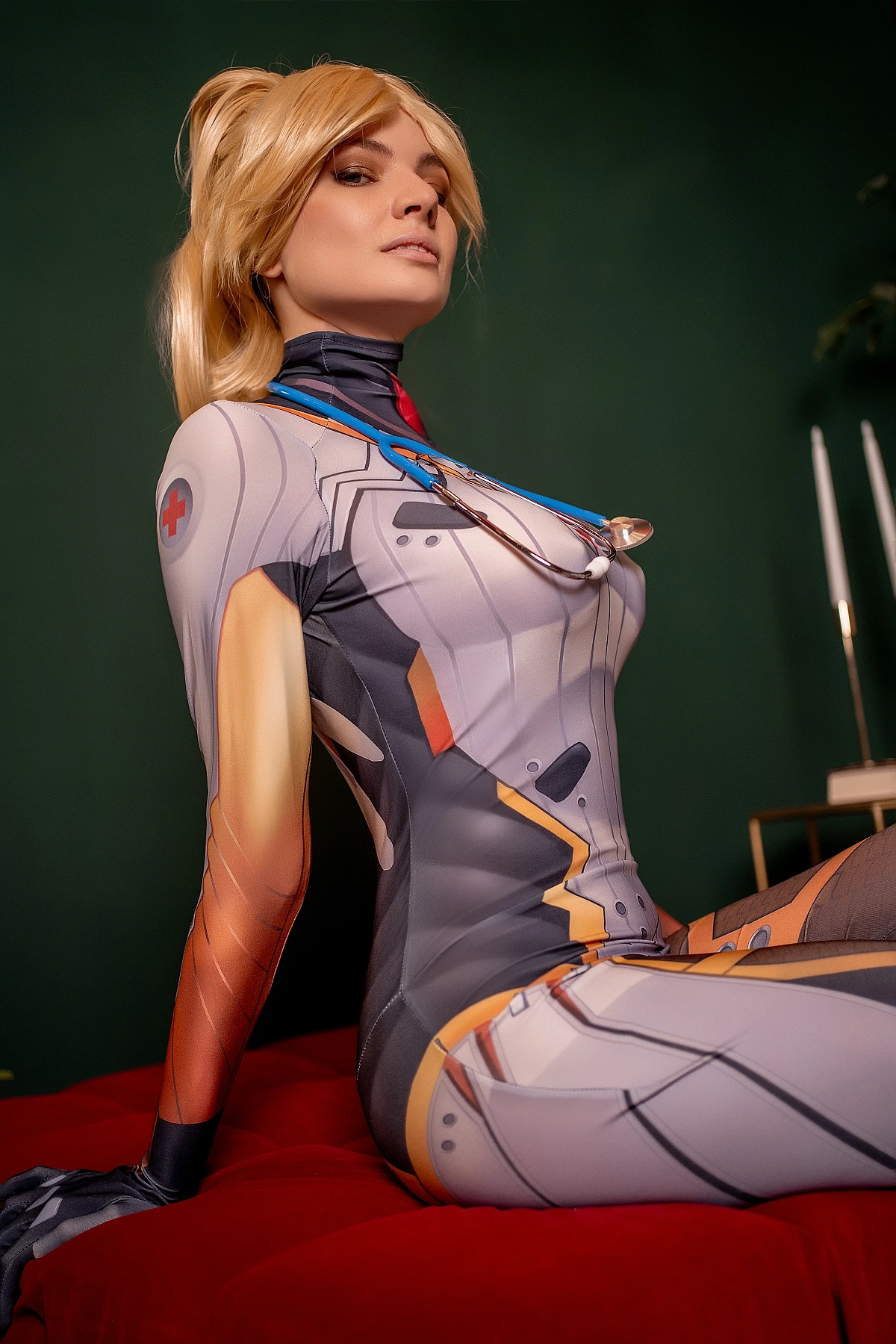 Mercy Overwatch cosplay leaning back on red bench, form-fitting white medical suit, stethoscope, dark emerald backdrop
