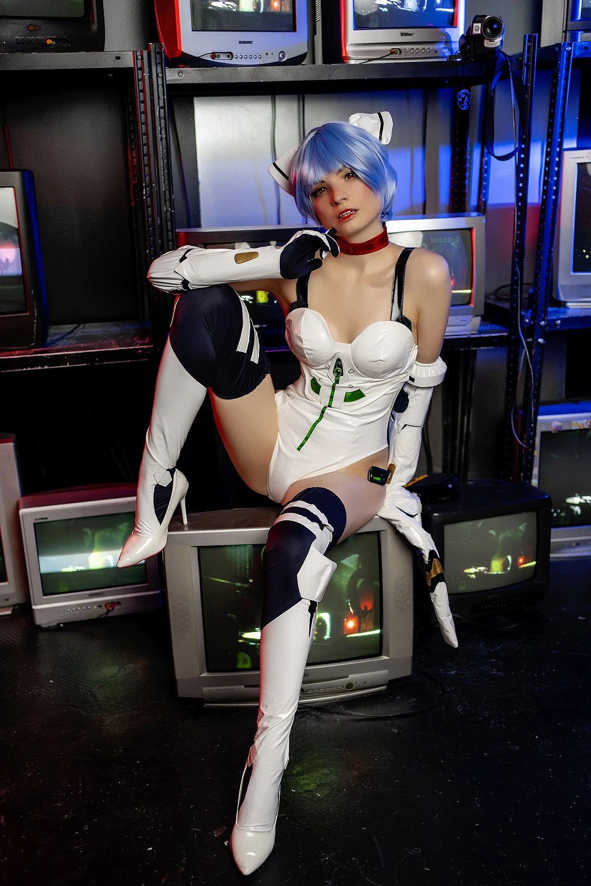 Rei Ayanami cosplay seated among CRT monitors wearing white EVA plugsuit with neon lighting